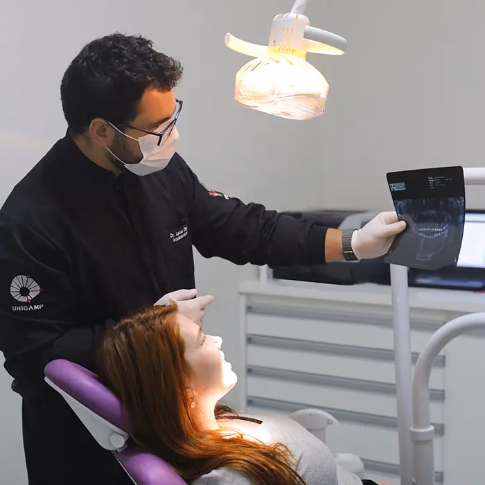 Dentista parceiro da Med Anchieta mostrando uma radiografia para uma paciente no consultório