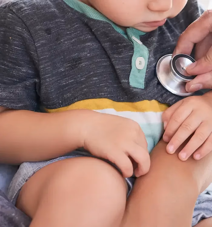 Pediatra examinando um bebê com o estetoscópio, no colo do responsável