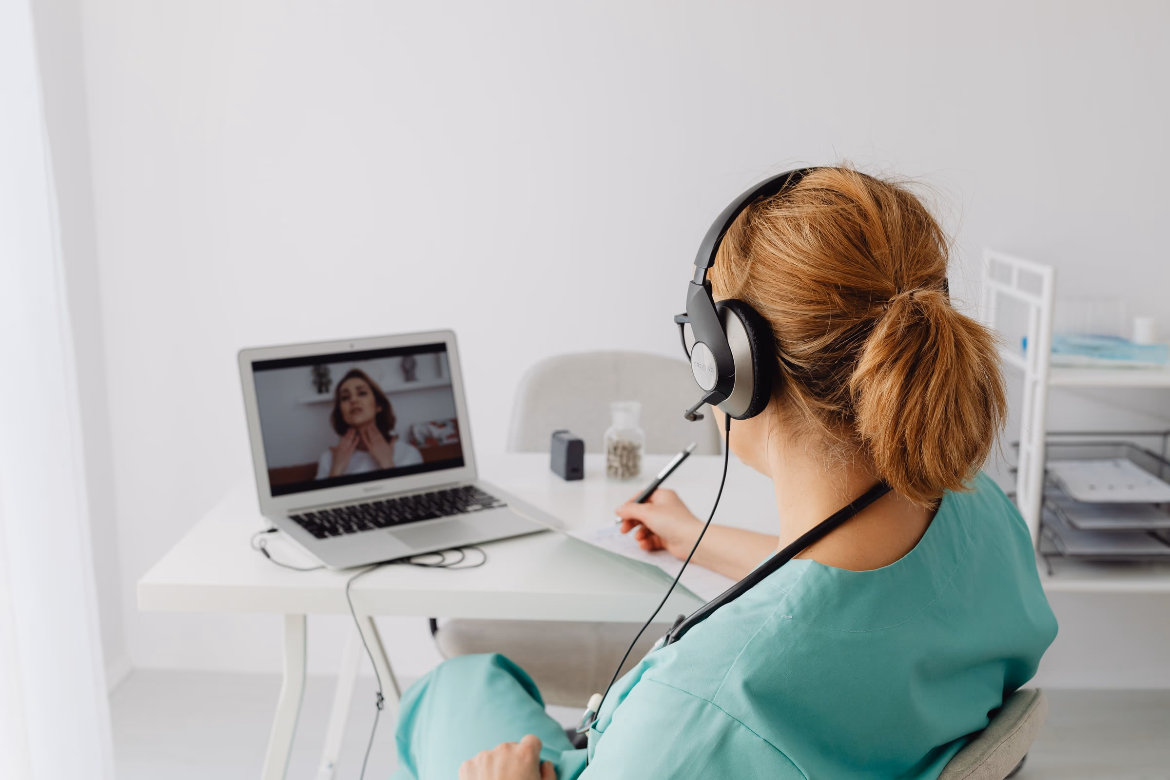 Profissional de saúde em consulta por vídeo, com a paciente visível na tela do notebook