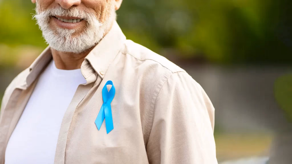 Laço azul de conscientização sobre o câncer de próstata preso à camisa de um homem sorrindo
